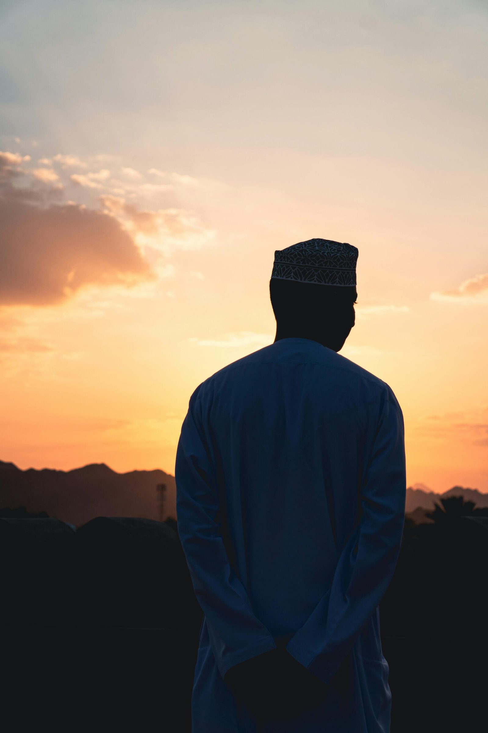 Silhouette of an Omani man in traditional attire overlooking a sunset in Nizwa, Oman.